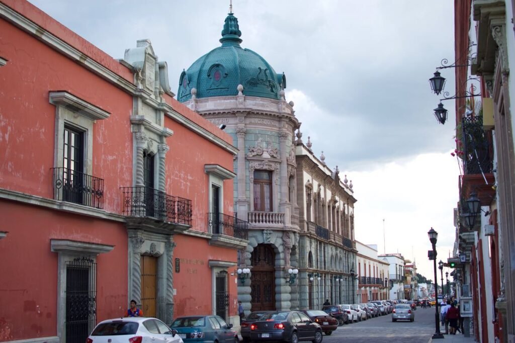 Historic buildings, parked cars and pedestrians on a central Oaxaca City street