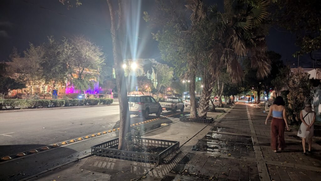 Pedestrians walking along the sidewalk beside Paseo de Montejo in Mérida at night