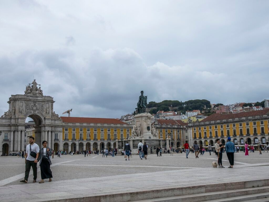People crossing Praça do Comércio in Lisbon with the Rua Augusta Arch and hillside behind