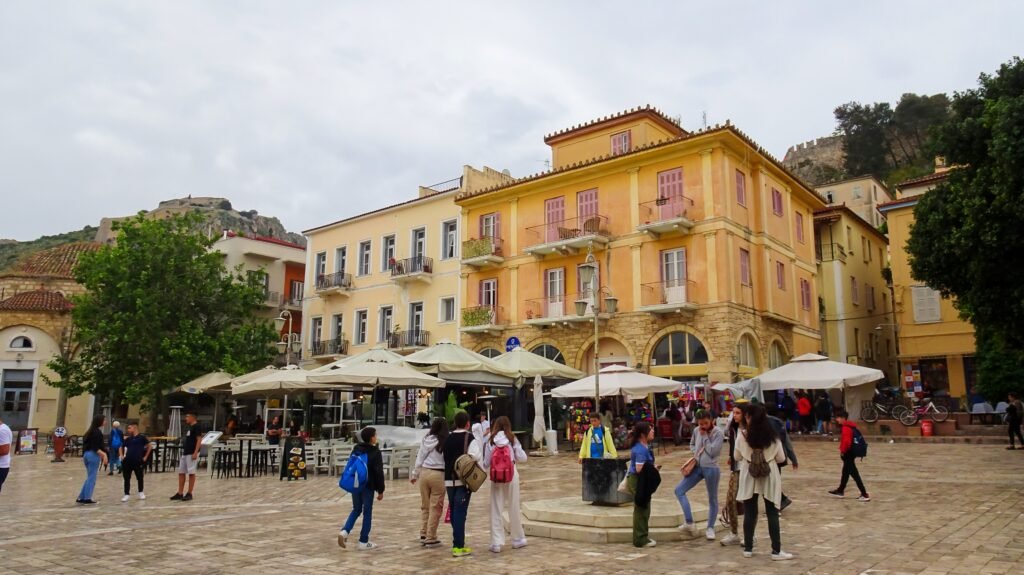 Syntagma Square in Nafplio Old Town with pedestrians, cafés and fortress slopes behind