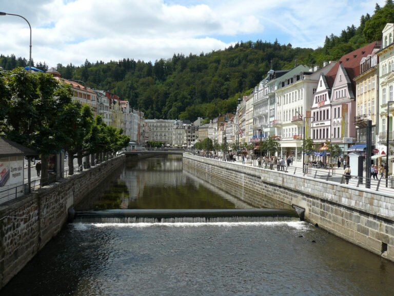 Teplá River promenade in Karlovy Vary with pedestrians, bridges and spa buildings along both banks